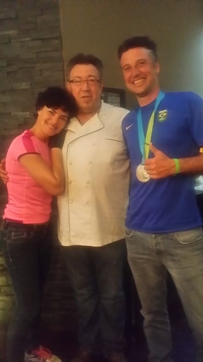 The chef in a white jacket with two guests; one wears a medal