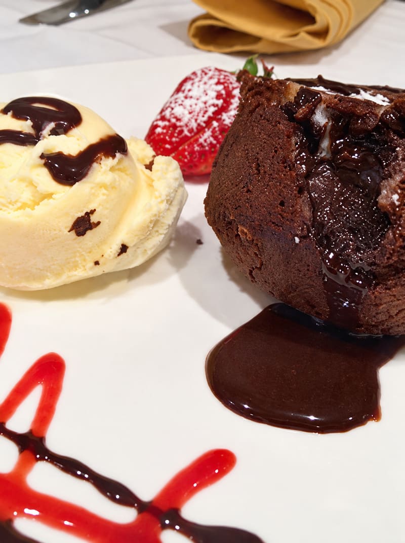 A dark chocolate cake with vanilla ice cream, a strawberry and chocolate sauce