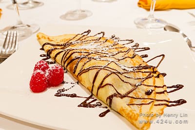 A folded pastry drizzled with chocolate, with raspberries and icing sugar