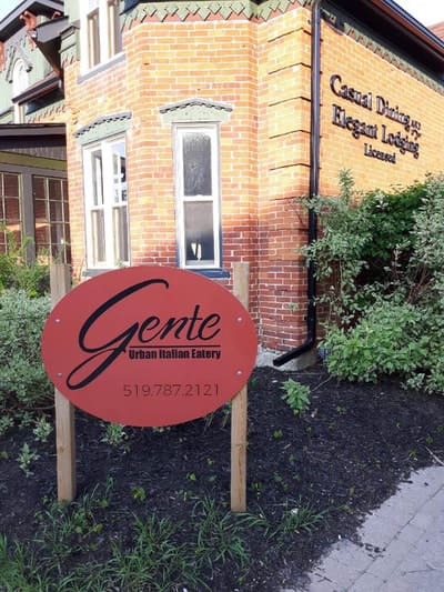 The red oval Gente sign in the garden in front of the brick building