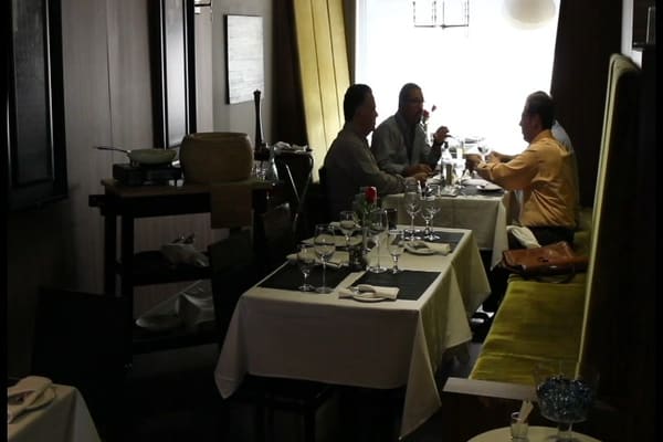 Three diners at a white-clothed table by a bright window, next to a green banquette
