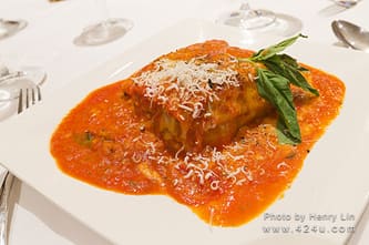 A square of lasagna in tomato sauce, topped with grated cheese and basil