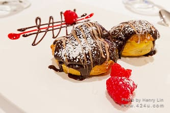 Cream puffs drizzled with chocolate, with raspberries and a sauce design