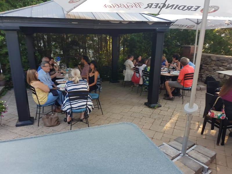 Another view of the patio, with guests at tables under umbrellas and a dark pergola