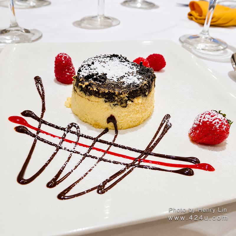 A round cake on a plate decorated with chocolate and raspberry sauce, with berries