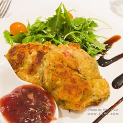 Two golden cakes with greens, a cherry tomato and a red relish