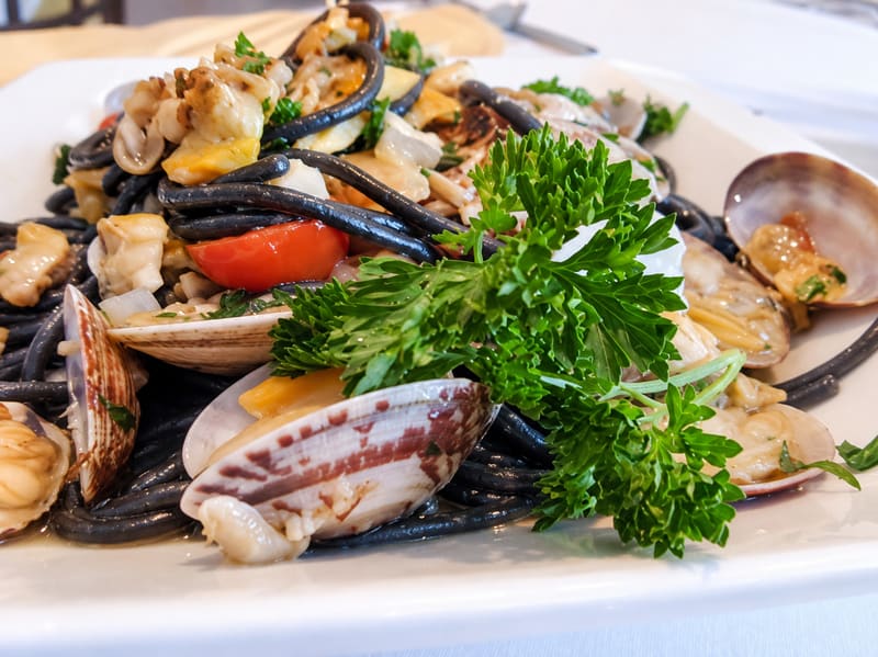 Dark pasta with clams, seafood, a cherry tomato and parsley