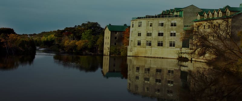 Old stone mill buildings beside a calm river, with autumn trees