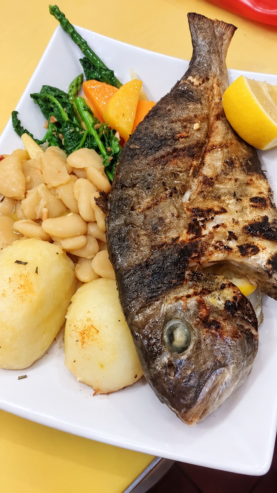 A whole grilled fish with white beans, potatoes, greens and lemon